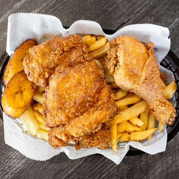 Crispy fried chicken pieces, golden french fries, and plantains served in a black basket.
