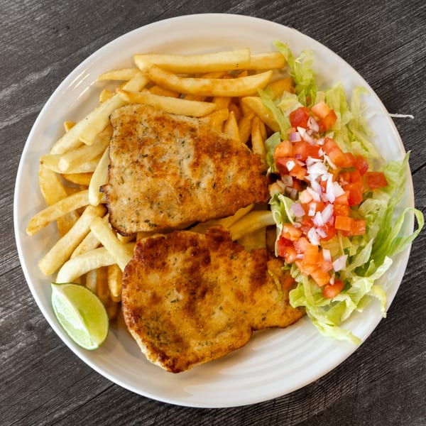 Two golden-brown chicken cutlets with french fries, a lime wedge, and a side salad.